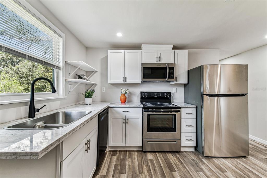 A kitchen features white cabinets, stainless steel appliances, a sink, and wood-look flooring — 1006 E 26TH AVENUE UNIT 1, TAMPA, FL