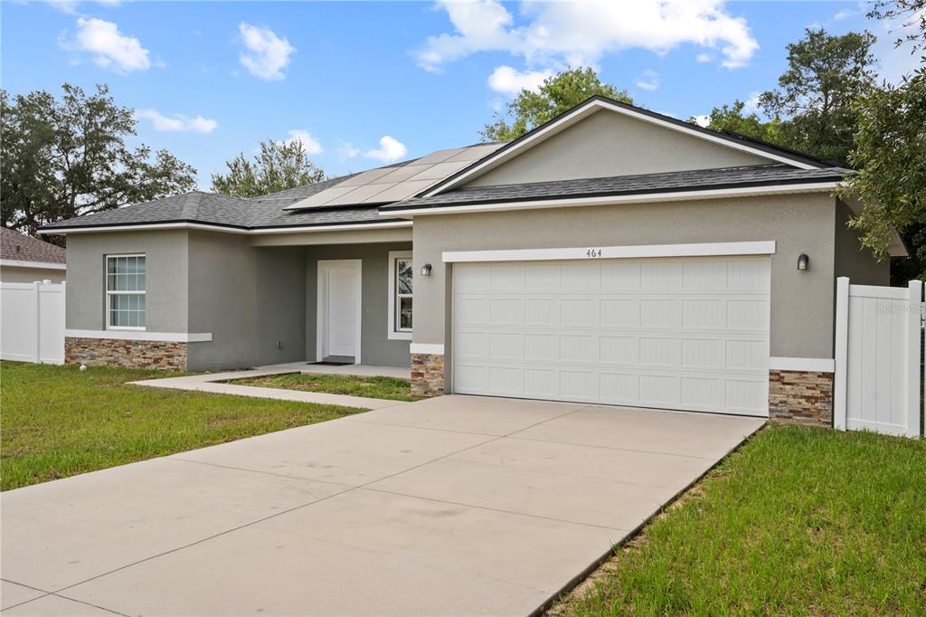 A single-story house with a white garage door, gray stucco siding, and solar panels — 464 DANUBE DRIVE, POINCIANA, FL