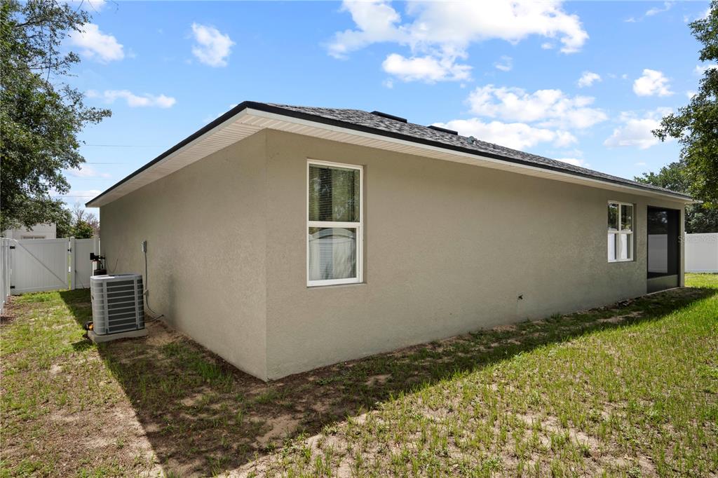 The exterior side of a tan stucco house features a window and an air conditioner — 464 DANUBE DRIVE, POINCIANA, FL