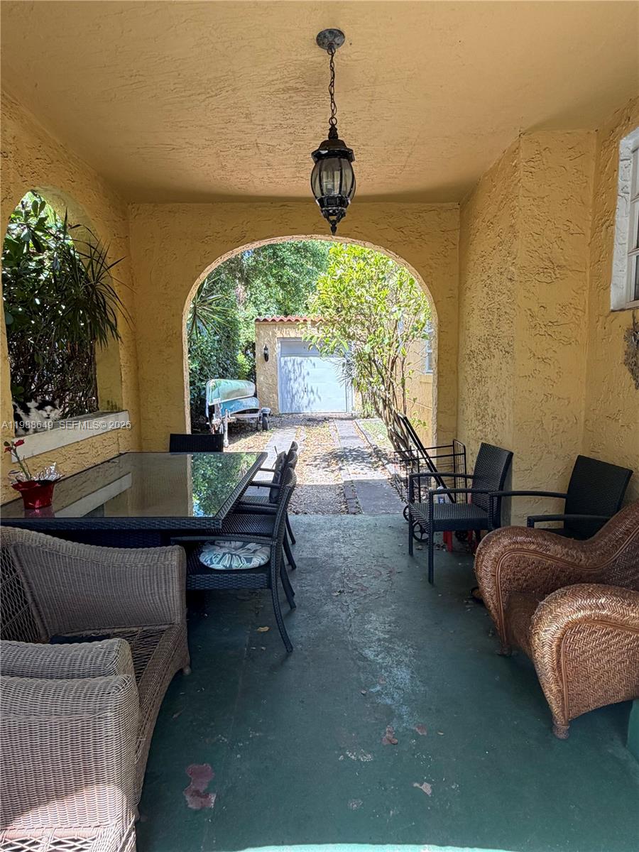 A covered patio features a dining set, wicker furniture, and a view of a detached garage — 1209 Mariana Ave, Coral Gables FL 33134, CORAL GABLES, FL