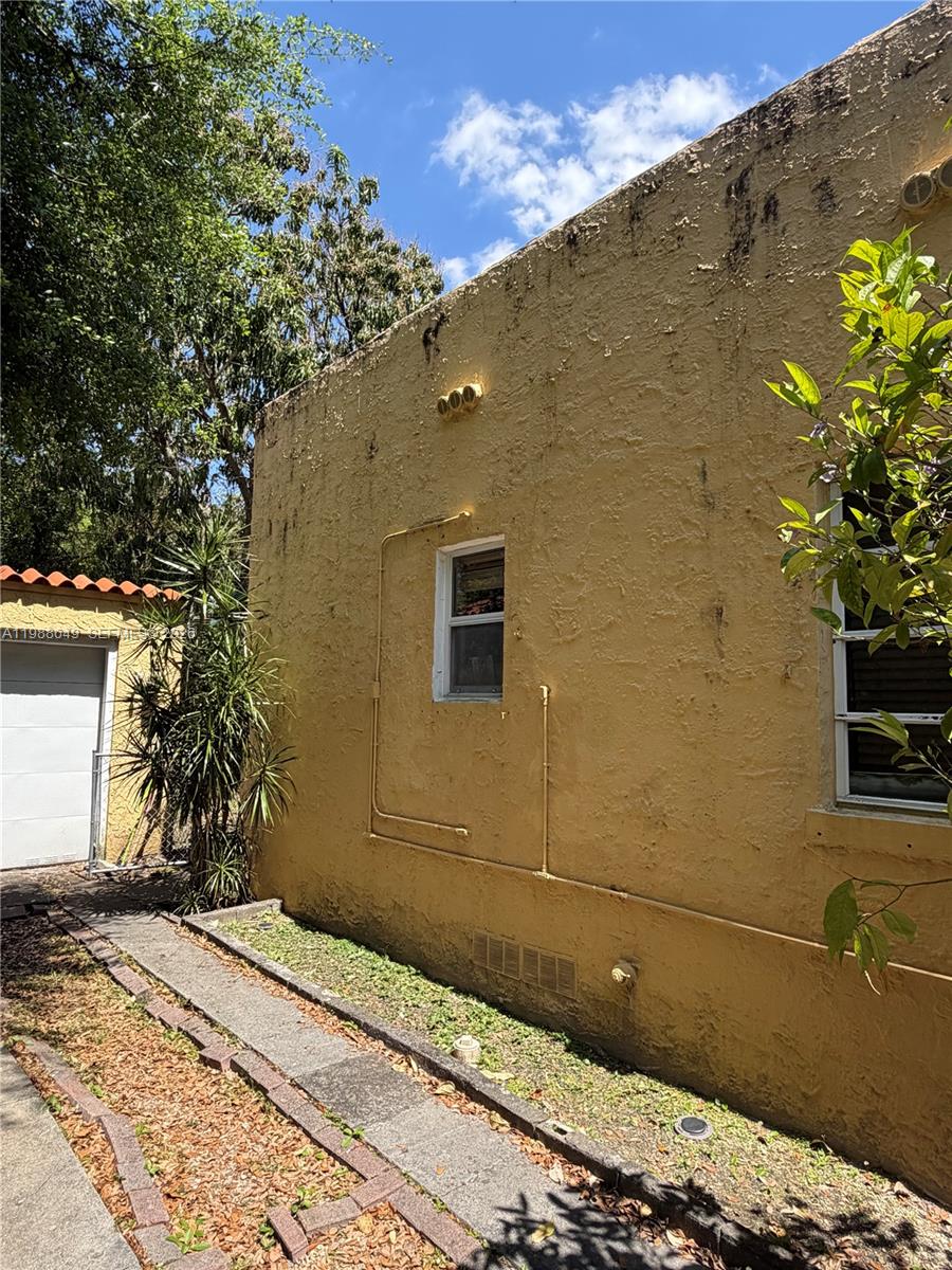 The exterior of a yellow stucco building features a small window and exposed pipes — 1209 Mariana Ave, Coral Gables FL 33134, CORAL GABLES, FL