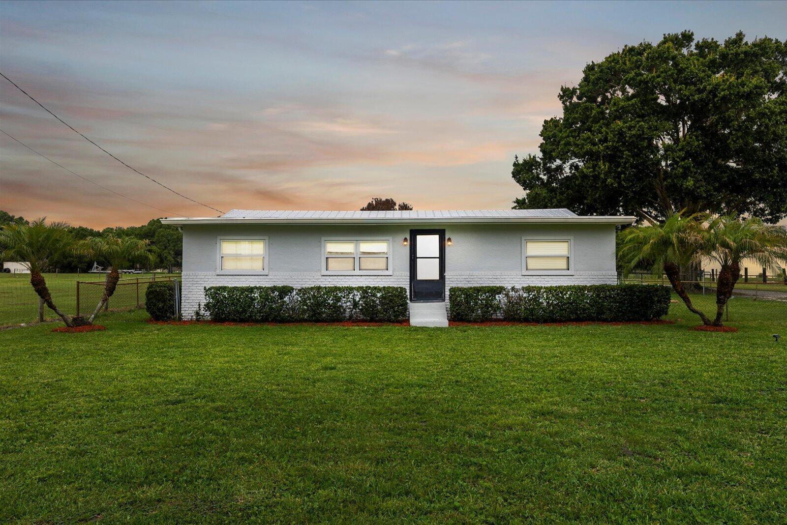A single-story white house with a metal roof sits on a grassy lawn — 6635 58th Avenue, Vero Beach FL 32967, VERO BEACH, FL