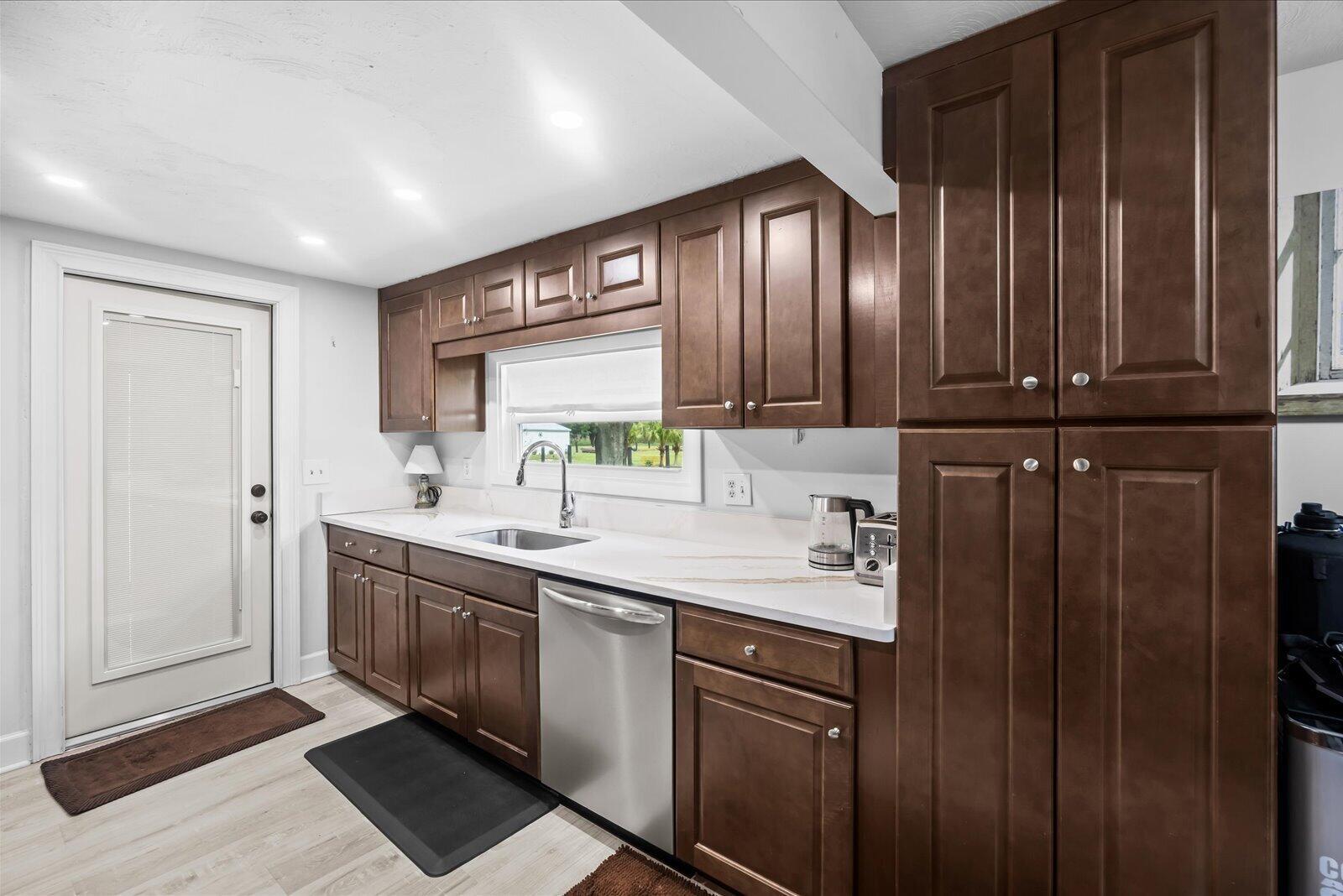 A kitchen with dark wood cabinets, white countertops, stainless steel appliances, and light wood flooring — 6635 58th Avenue, Vero Beach FL 32967, VERO BEACH, FL