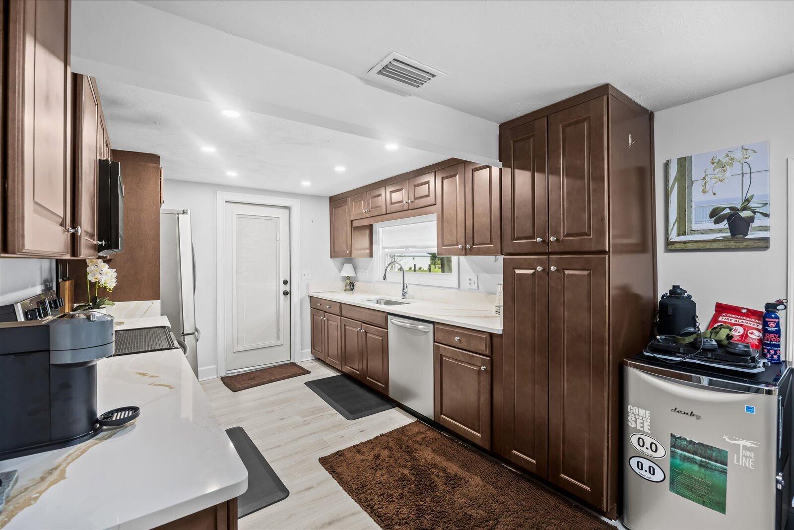 A kitchen features brown cabinets, white countertops, stainless steel appliances, and light wood-look flooring — 6635 58th Avenue, Vero Beach FL 32967, VERO BEACH, FL