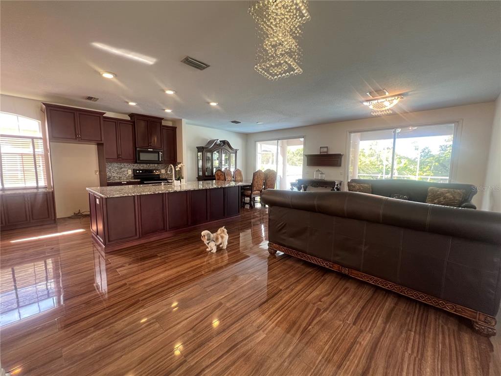 An open-concept kitchen and living area features dark wood cabinetry, granite countertops, and wood flooring — 6222 LAUREL CREEK TRAIL, ELLENTON, FL