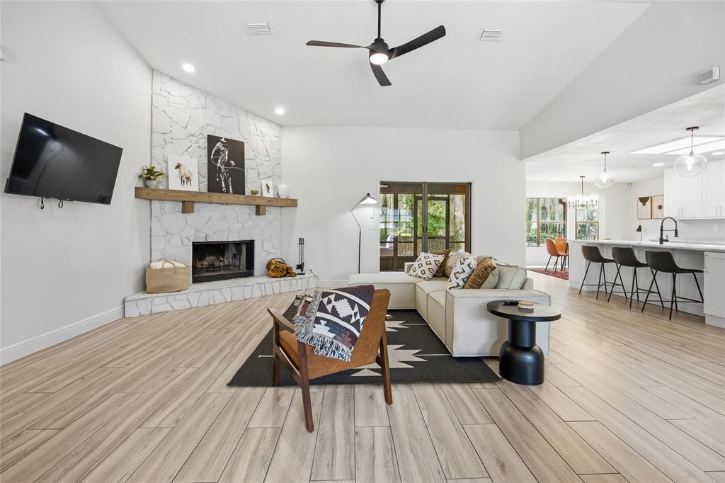 A living room features a white stone fireplace, wood-look flooring, and an open kitchen area — 8274 NW 47TH STREET, OCALA, FL