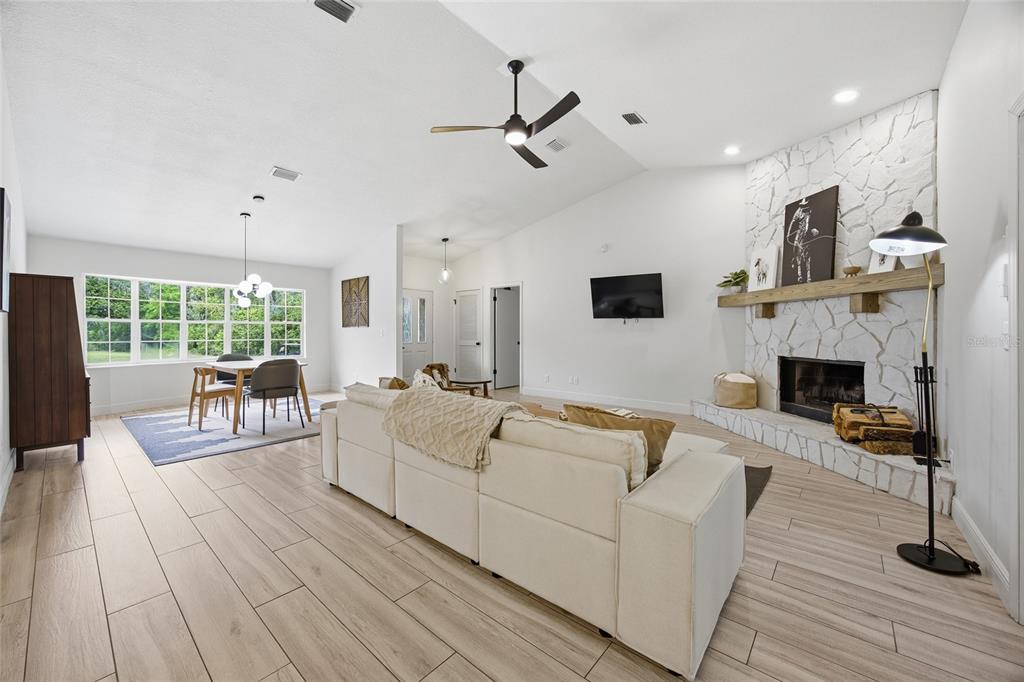 A bright living and dining area features white stone fireplace, light wood flooring, and vaulted ceilings — 8274 NW 47TH STREET, OCALA, FL