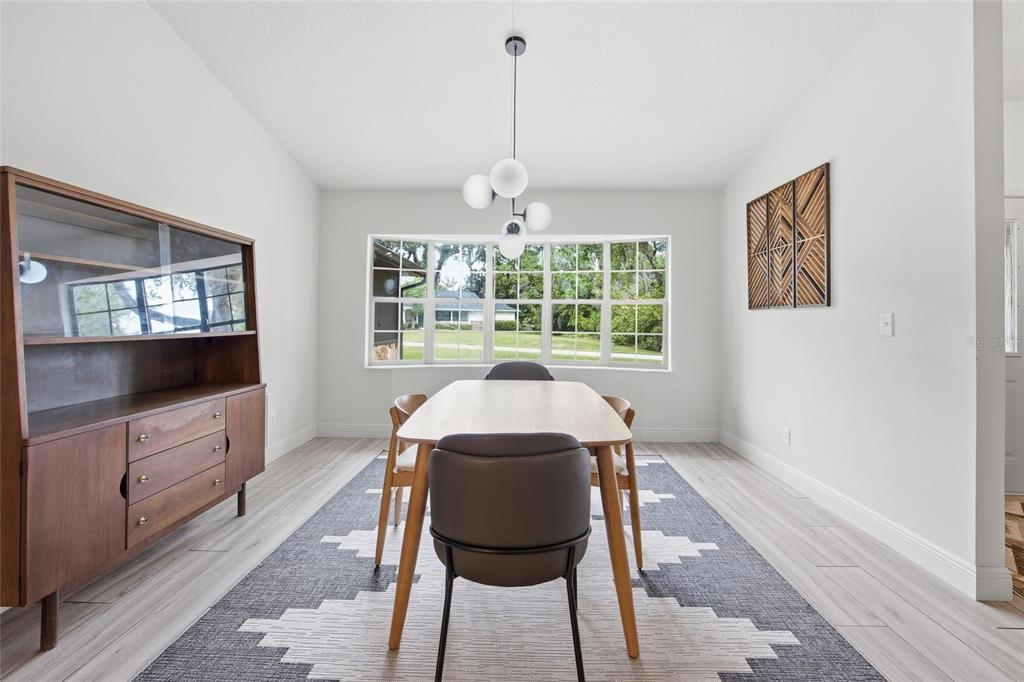 A dining room features a wooden table, mid-century hutch, geometric rug, and a large window — 8274 NW 47TH STREET, OCALA, FL