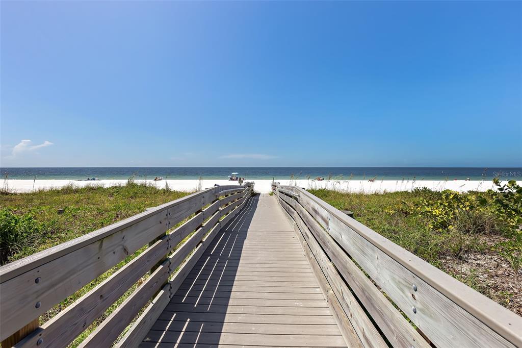 A wooden boardwalk leads through dunes to a sandy beach under a clear blue sky — 16333 GULF BOULEVARD UNIT 113, REDINGTON BEACH, FL