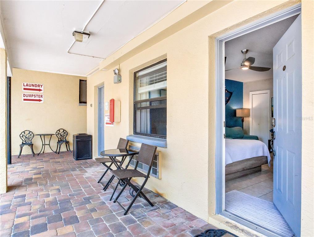 A paved outdoor patio with seating leads into a bedroom through an open door — 16333 GULF BOULEVARD UNIT 113, REDINGTON BEACH, FL