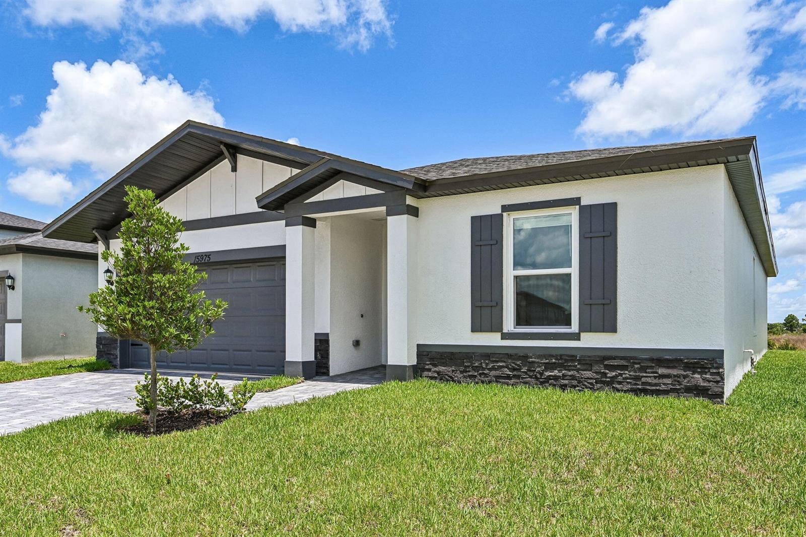 A single-story house with white stucco, dark gray trim, stone accents, and a paved driveway — 15975 SW Vine Drive, FL 34956, FL