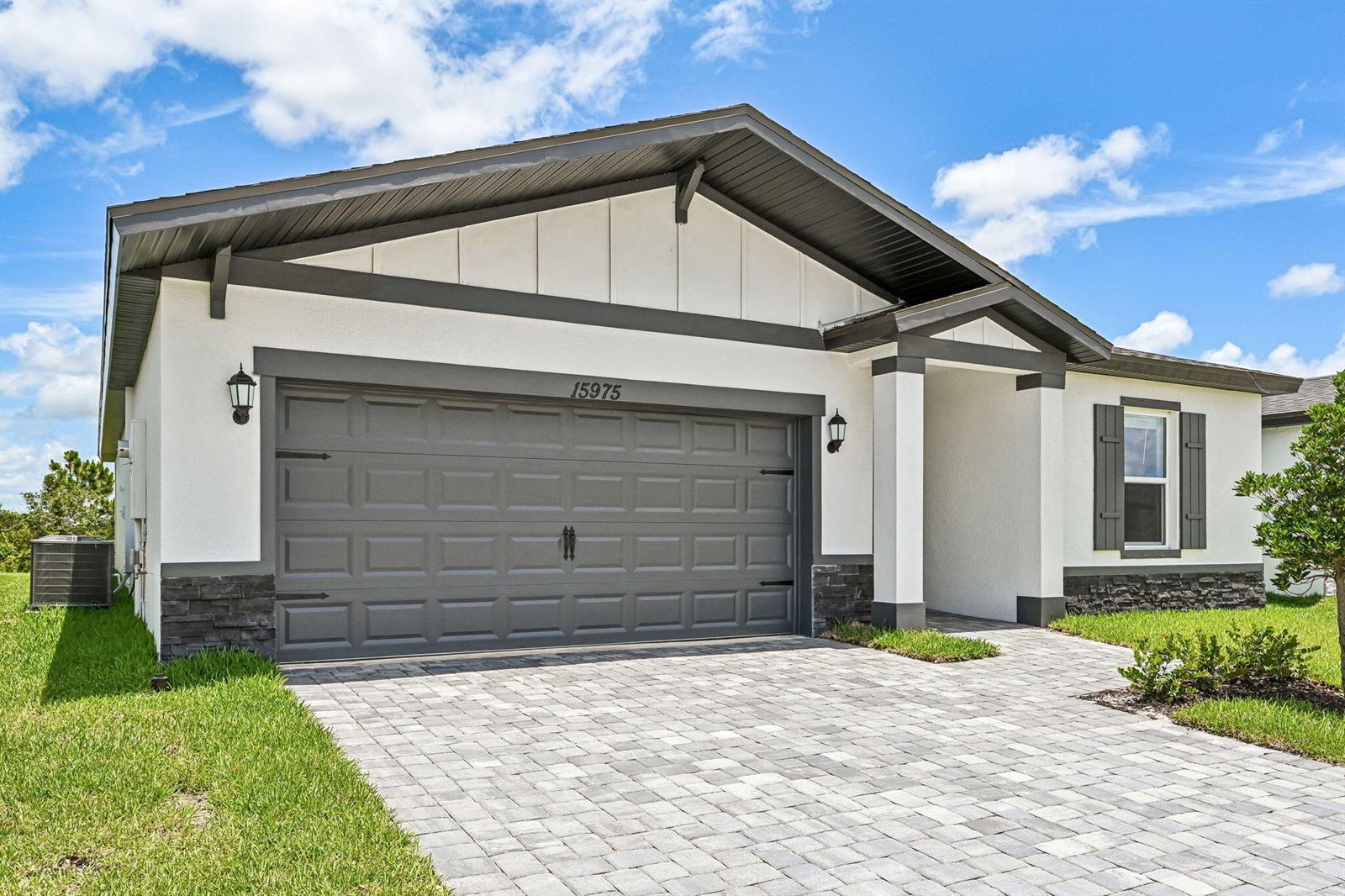A single-story house exterior features a gray garage door, white stucco walls, and stone accents — 15975 SW Vine Drive, FL 34956, FL