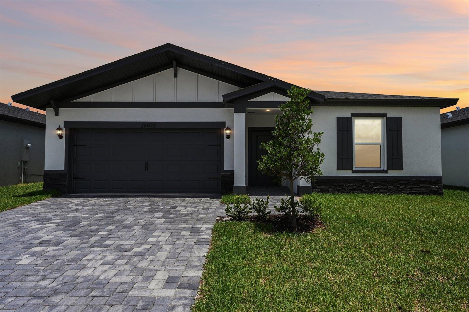 A single-story house with a dark garage door, stone accents, and a paved driveway — 15975 SW Vine Drive, FL 34956, FL
