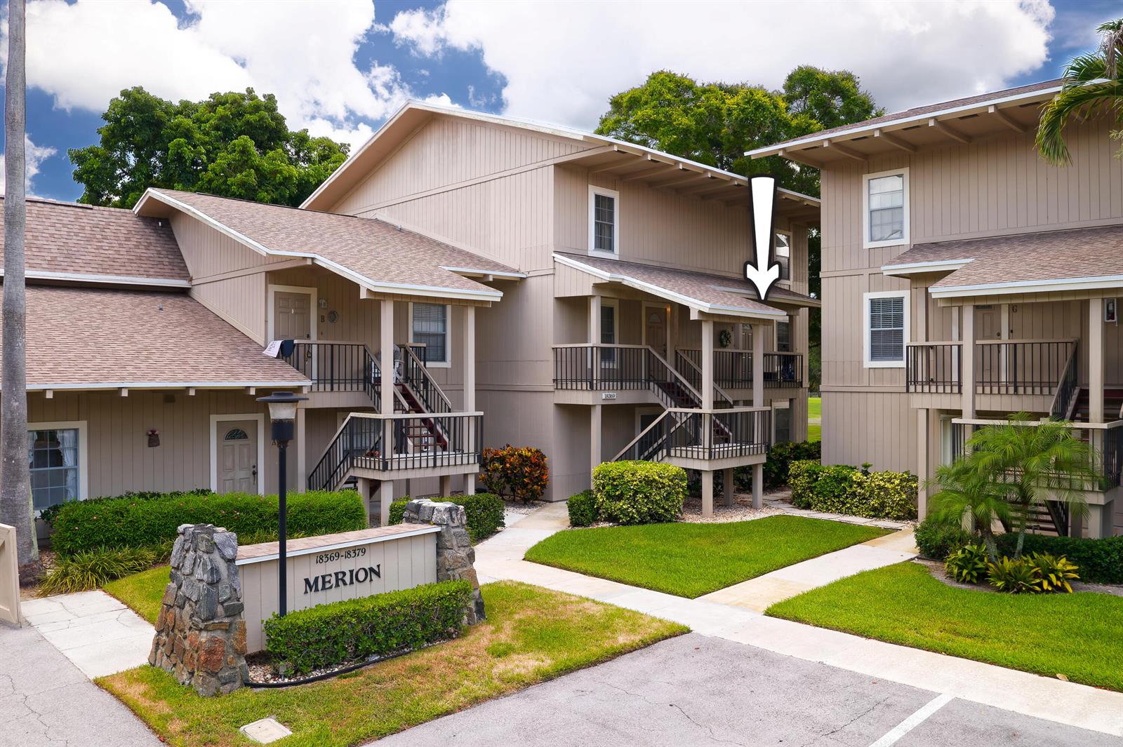 Exterior view of multi-story apartment buildings with tan siding and a stone entrance sign — 18369 SE Wood Haven Lane, Jupiter FL 33469, JUPITER, FL
