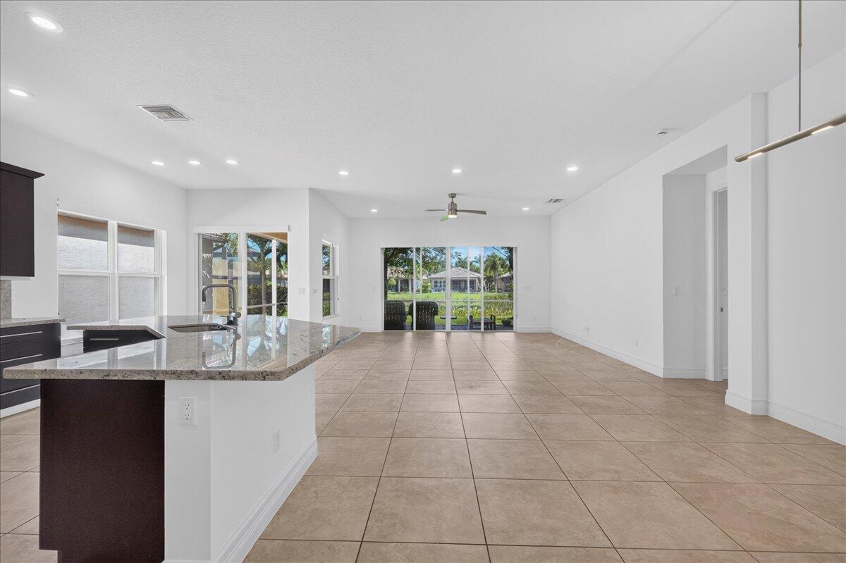 An open-concept kitchen and living area with tile flooring, granite countertops, and sliding glass doors — 8681 Cathedral Peak Court, Boynton Beach FL 33473, BOYNTON BEACH, FL