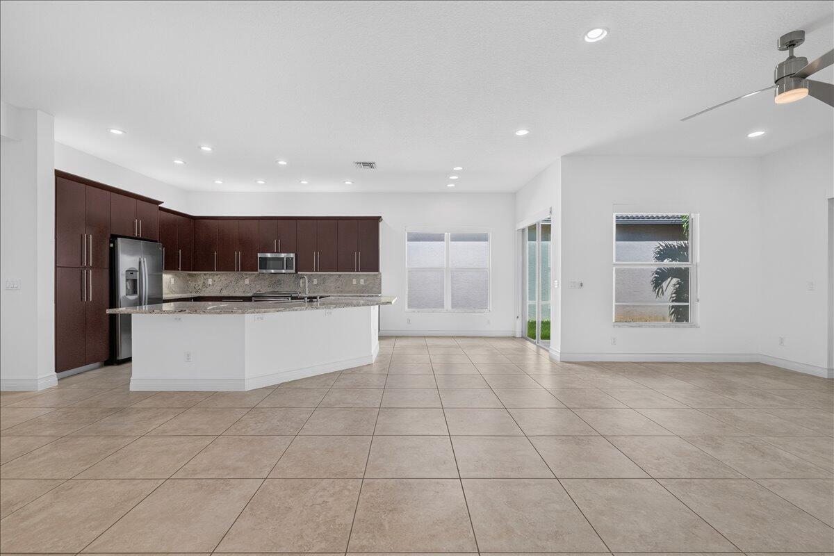 A kitchen with dark wood cabinets and a granite island opens to a tiled living area — 8681 Cathedral Peak Court, Boynton Beach FL 33473, BOYNTON BEACH, FL