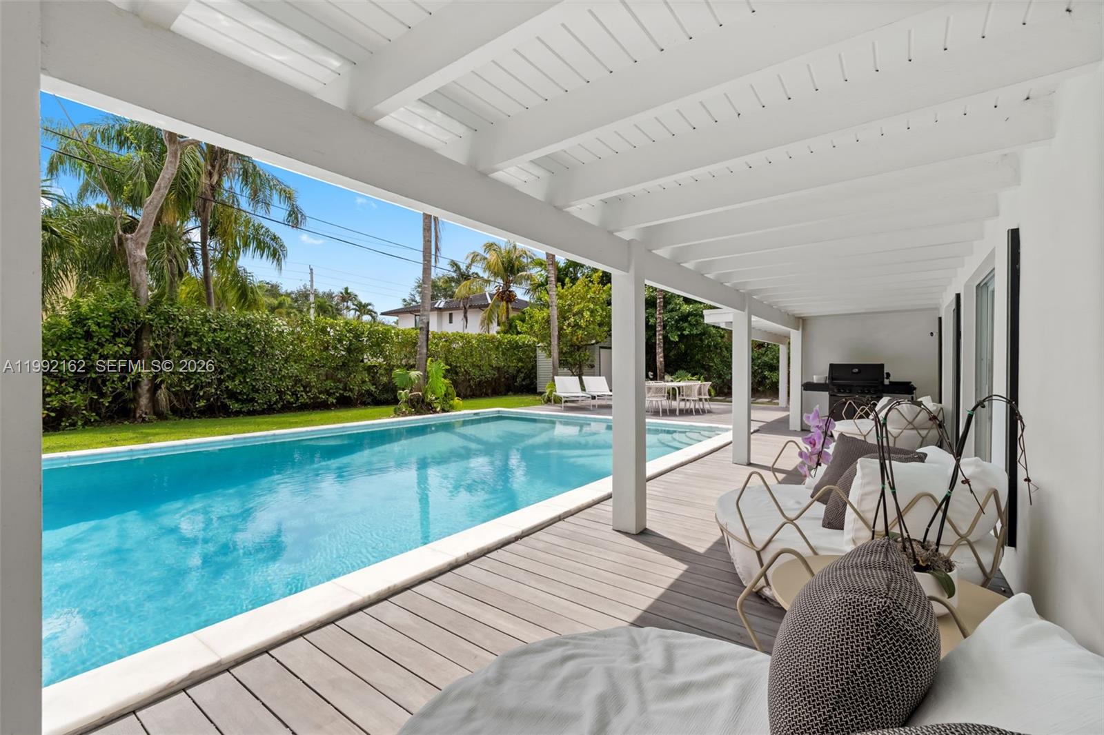 A covered wooden deck features outdoor seating overlooking a swimming pool and backyard — 7531 SW 52nd Ct, Miami FL 33143, MIAMI, FL