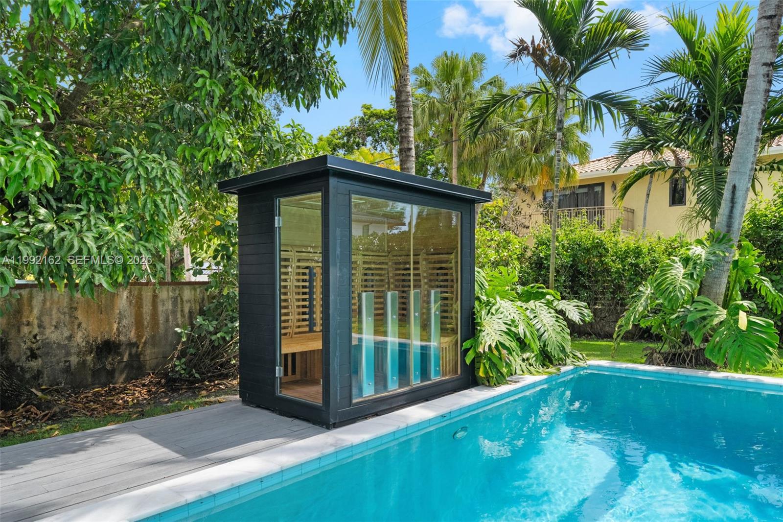 A modern outdoor sauna with glass walls sits on a deck beside a swimming pool — 7531 SW 52nd Ct, Miami FL 33143, MIAMI, FL