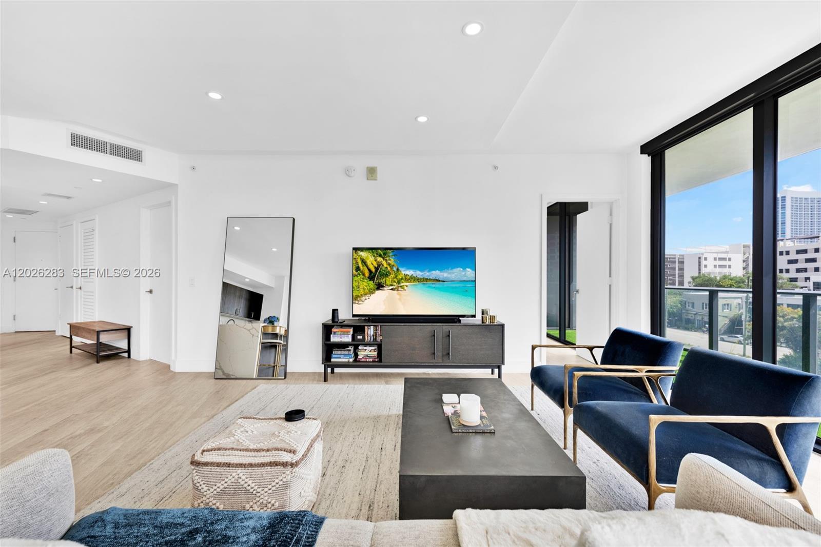 A modern living room features a television console, blue armchairs, and a large floor mirror — 121 NE 34th St # L304, Miami FL 33137, MIAMI, FL
