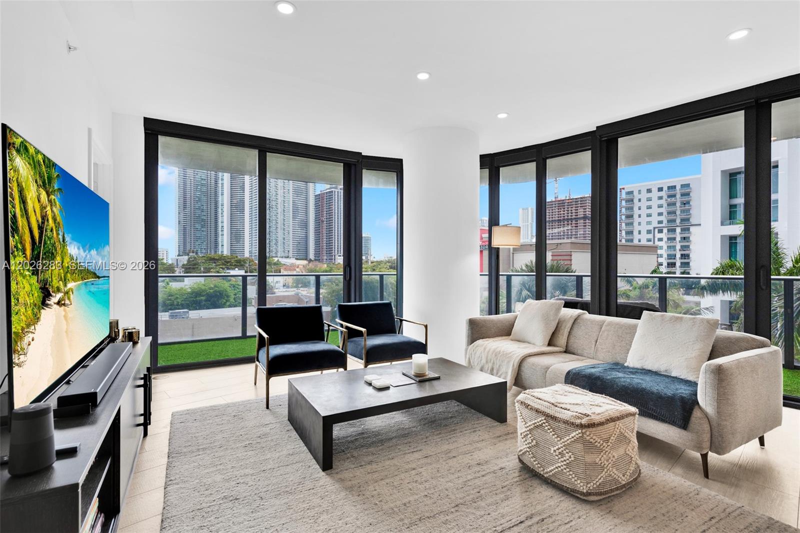 A modern living room features floor-to-ceiling windows, a grey sofa, and a city view — 121 NE 34th St # L304, Miami FL 33137, MIAMI, FL