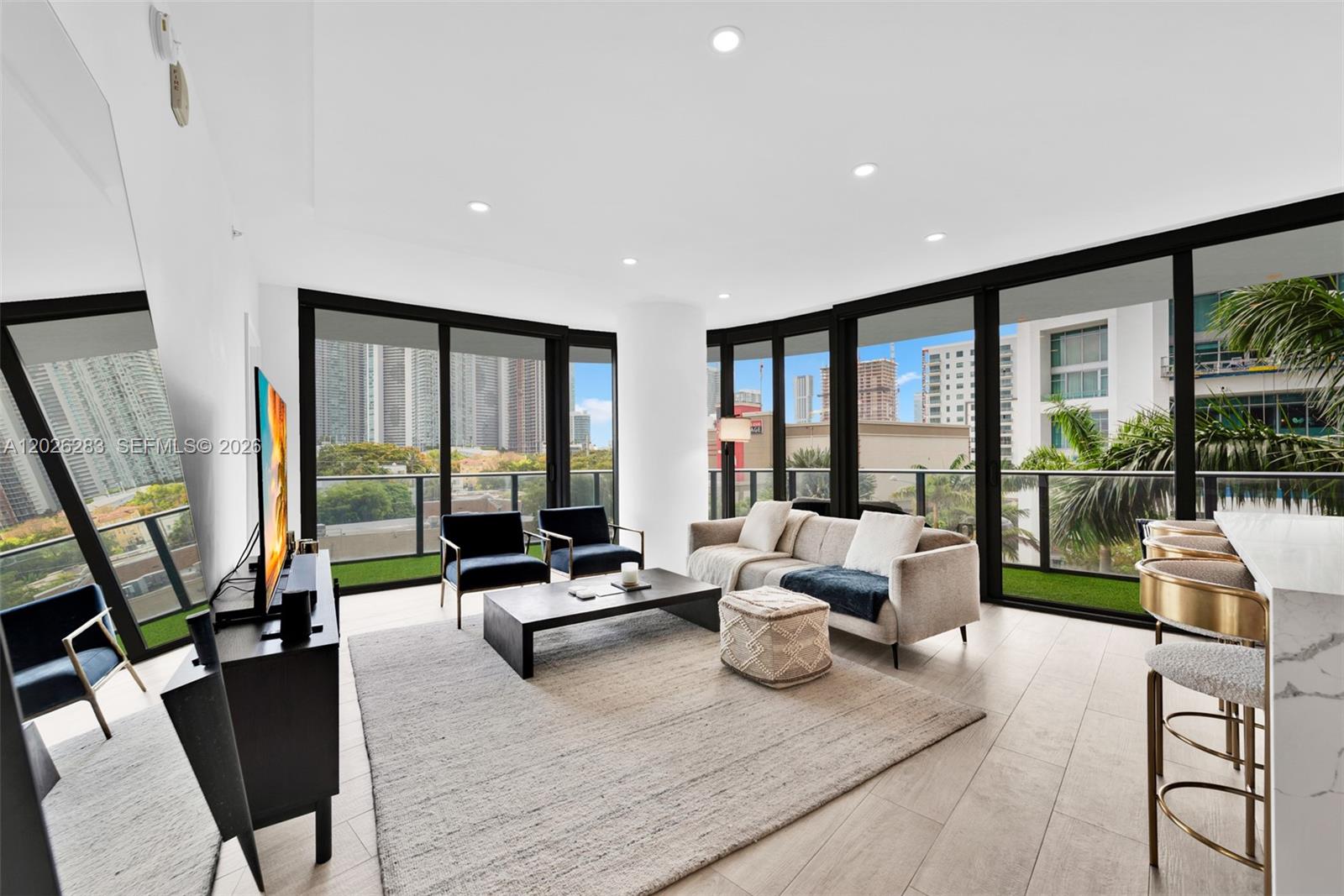 A modern living room features floor-to-ceiling windows, light wood flooring, and a balcony with city views — 121 NE 34th St # L304, Miami FL 33137, MIAMI, FL