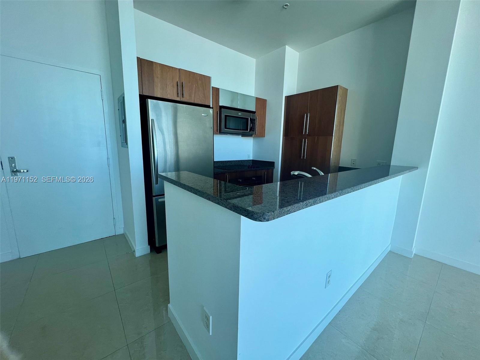 A kitchen features a granite breakfast bar, stainless steel refrigerator, and wood-toned cabinetry — 300 S Biscayne Blvd # 3907, Miami FL 33131, MIAMI, FL
