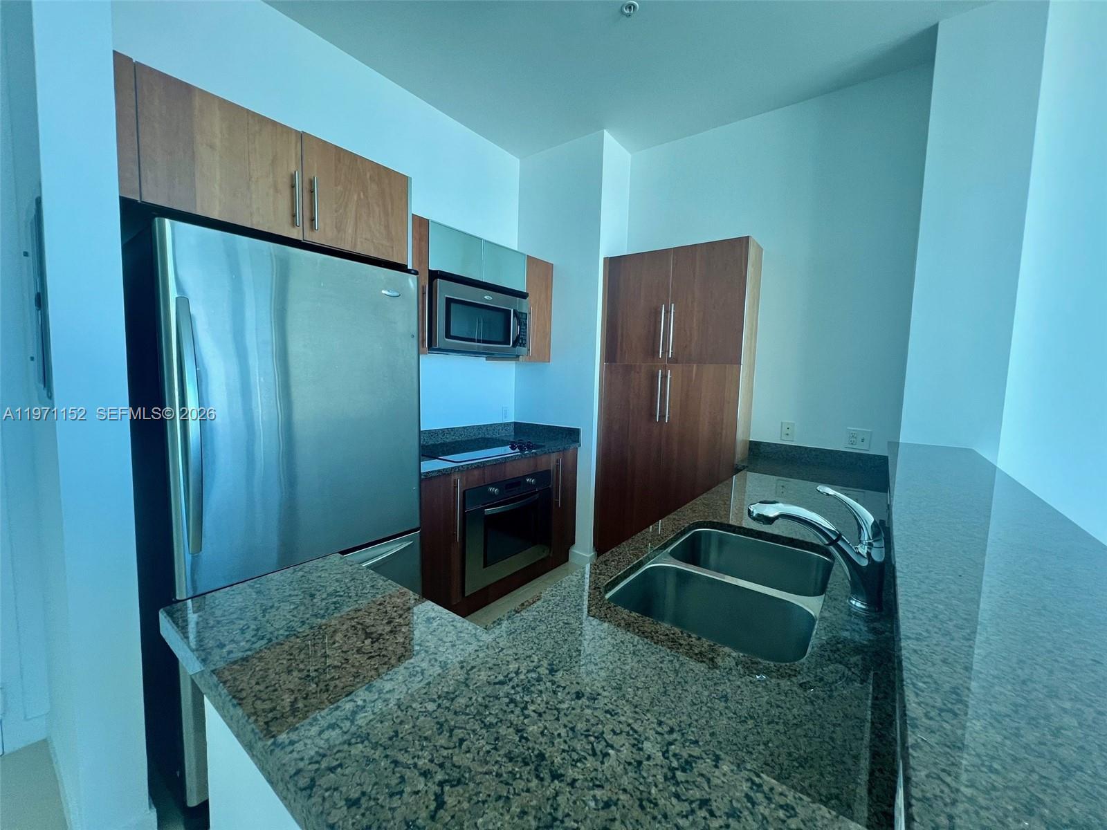 A kitchen features stainless steel appliances, wood cabinetry, and dark granite countertops — 300 S Biscayne Blvd # 3907, Miami FL 33131, MIAMI, FL