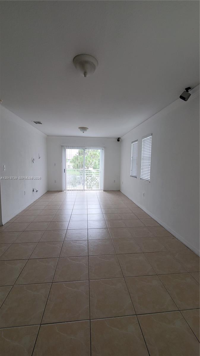 An empty room features white walls, beige tile flooring, and a sliding glass door — 8804 NW 109th Pl # 402, Doral FL 33178, DORAL, FL