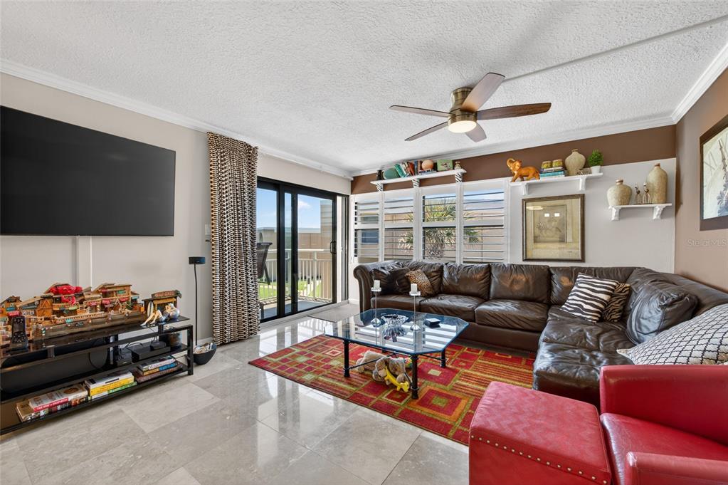 A living room features a brown leather sectional, a glass coffee table, and tile flooring — 4811 SAXON DRIVE UNIT A-203, NEW SMYRNA BEACH, FL