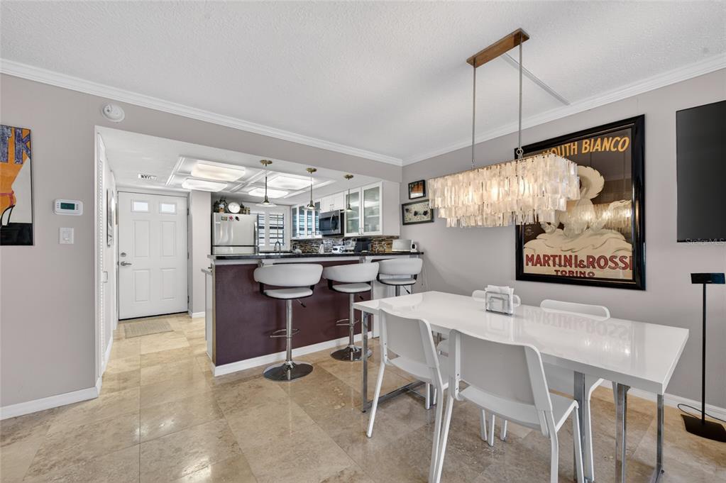 A dining area with a white table and chandelier sits adjacent to a kitchen bar — 4811 SAXON DRIVE UNIT A-203, NEW SMYRNA BEACH, FL