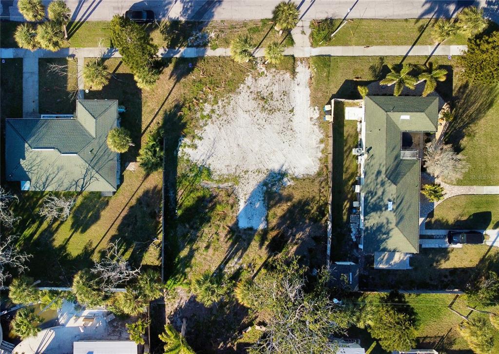 An aerial view shows a vacant, sandy residential lot situated between two houses with green roofs — 843 BRUCE AVENUE, CLEARWATER BEACH, FL