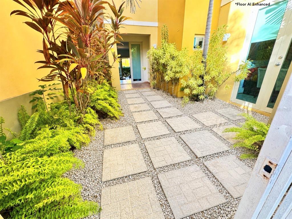 A stone paver walkway leads to a doorway between yellow walls and lush green plants — 90 CANDELERO DRIVE UNIT 120, HUMACAO, PR