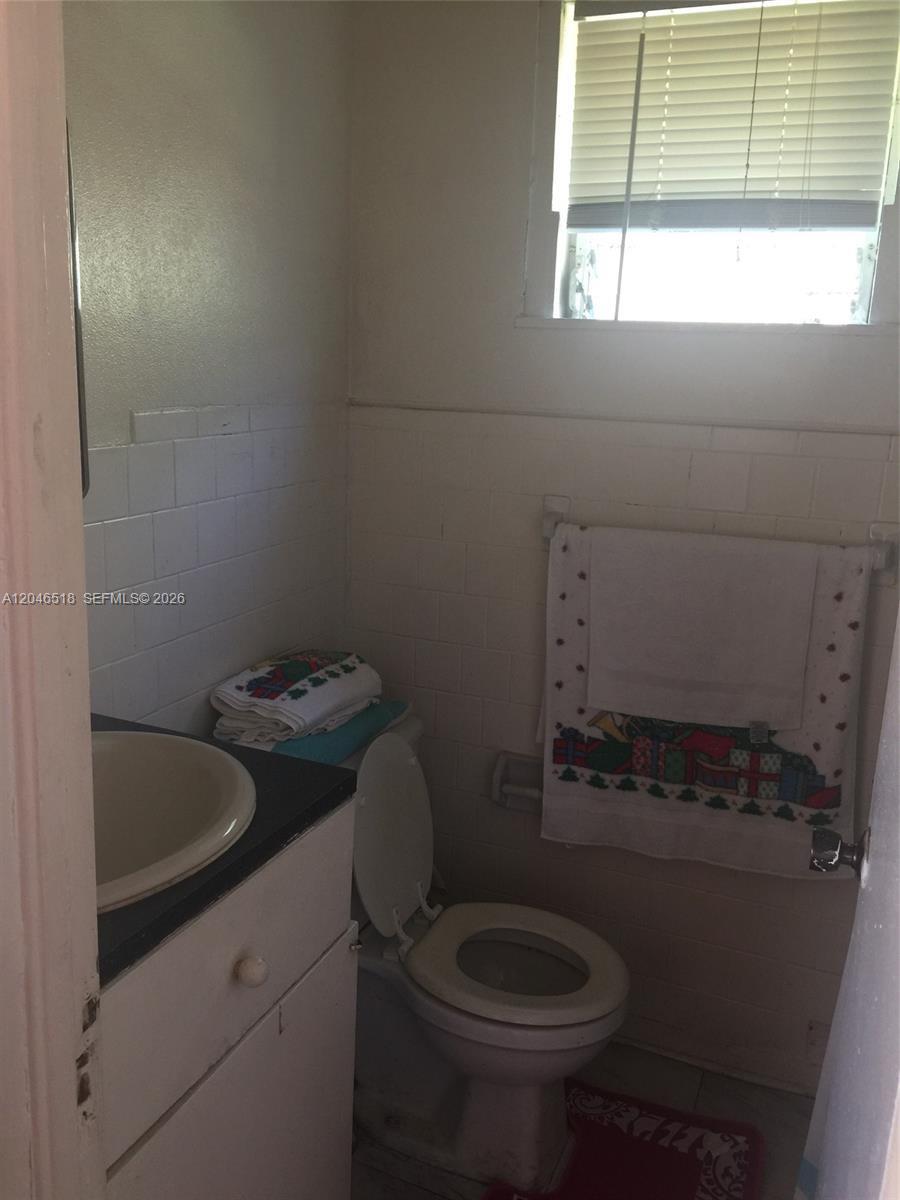 A small bathroom features a white vanity, a toilet, and white wall tiles — 22 SW 11th St, Dania Beach FL 33004, DANIA BEACH, FL