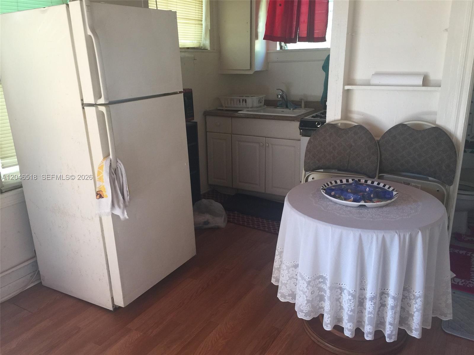 A small kitchen features a white refrigerator, a sink, wooden cabinets, and a dining table — 22 SW 11th St, Dania Beach FL 33004, DANIA BEACH, FL