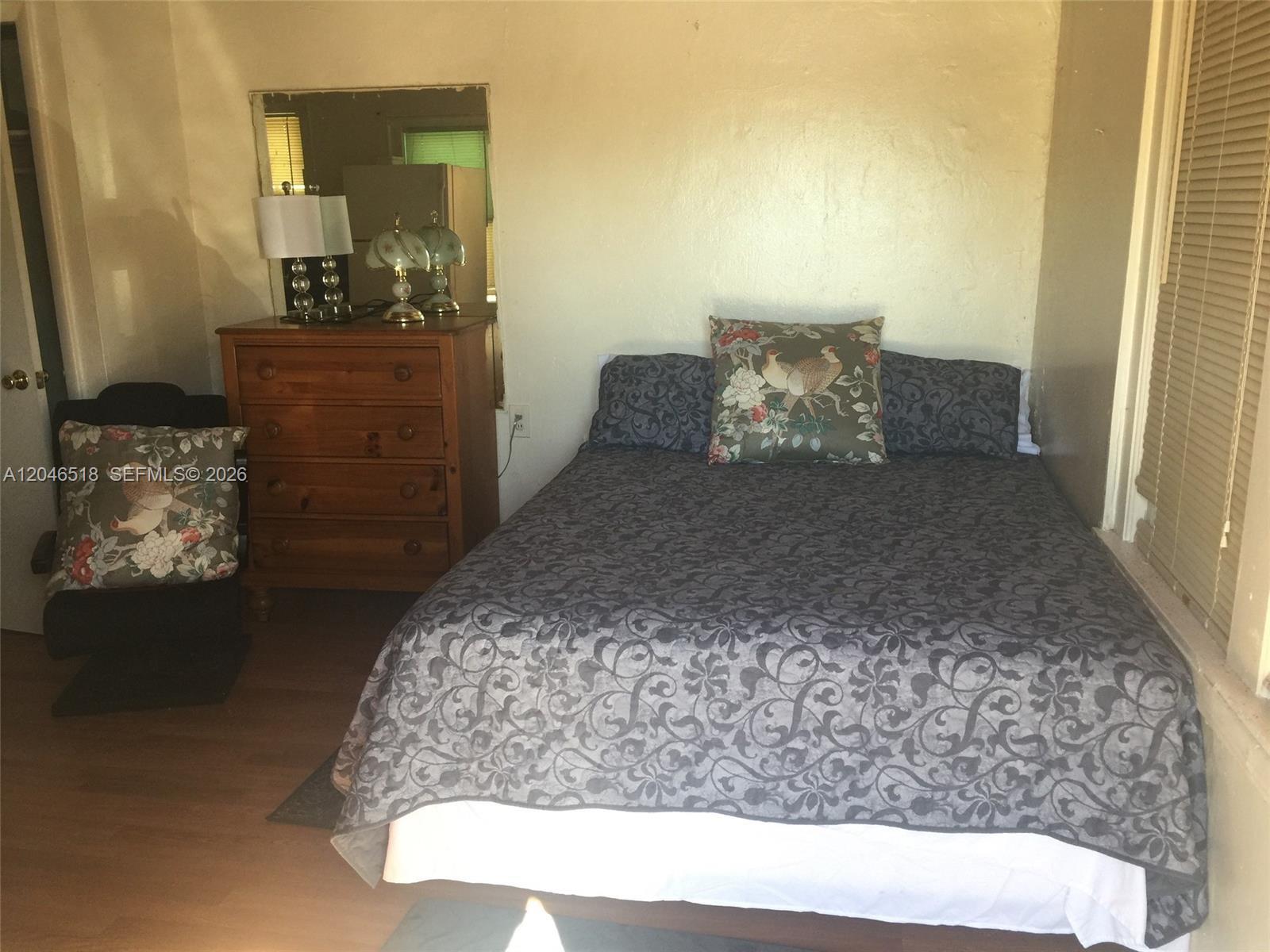 A bedroom features a bed with a patterned quilt, a wooden dresser, and a chair — 22 SW 11th St, Dania Beach FL 33004, DANIA BEACH, FL
