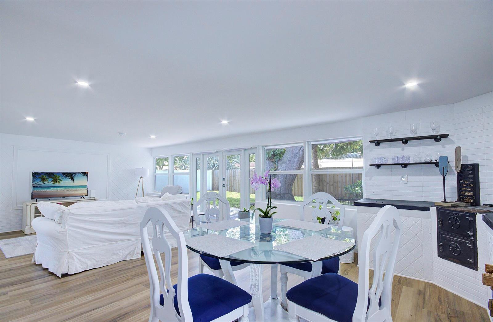A bright living and dining area features white furniture, a glass table, and wood flooring — 1950 NE 30th Street, Lighthouse Point FL 33064, LIGHTHOUSE POINT, FL
