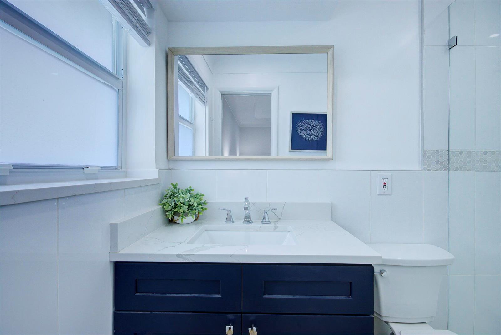 A bathroom features a dark blue vanity, white marble countertop, and a rectangular wall mirror — 1950 NE 30th Street, Lighthouse Point FL 33064, LIGHTHOUSE POINT, FL