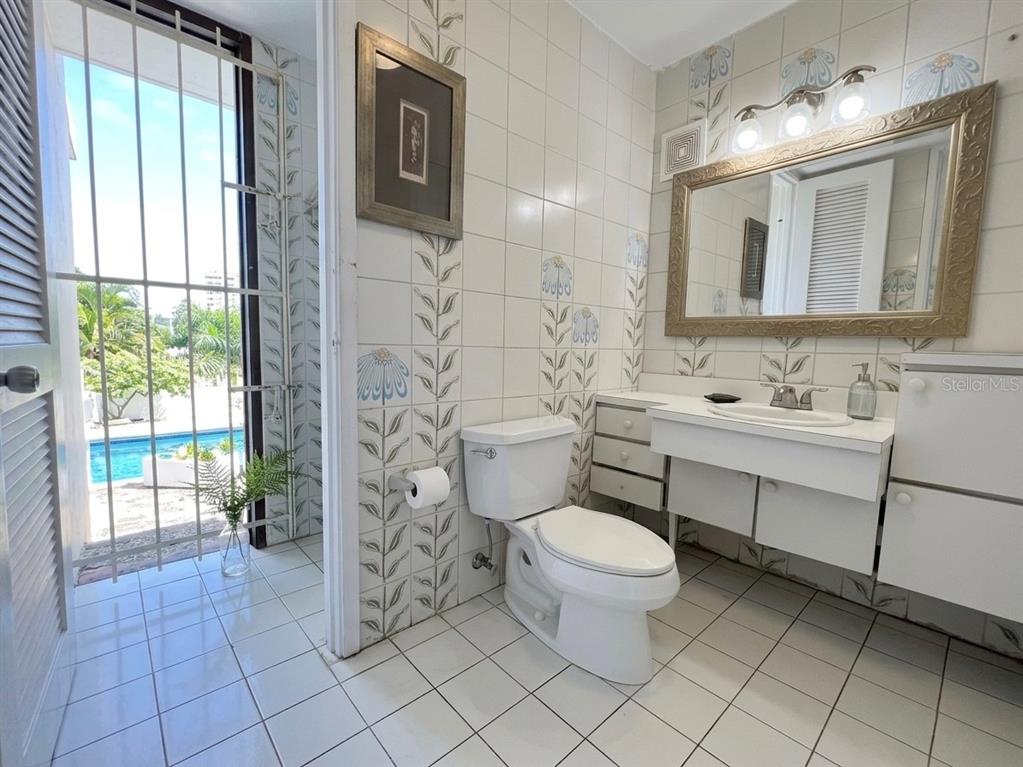 A bathroom with floral-patterned wall tiles, a white toilet, vanity, and a view of a pool — I 25 VILLA CAPARRA NOR, GUAYNABO, PR
