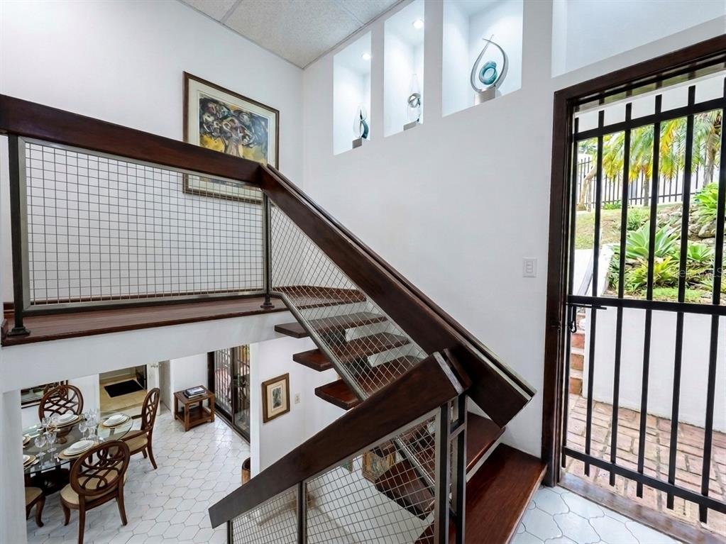 A staircase with wooden treads and a metal grid railing overlooks a dining area — I 25 VILLA CAPARRA NOR, GUAYNABO, PR
