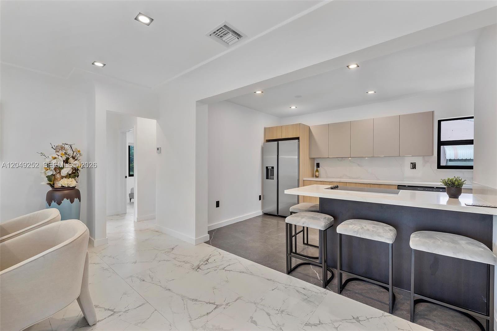 A modern kitchen features a dark island, light cabinetry, and white marble-style flooring — 501 NW 46th St # 0, Miami FL 33127, MIAMI, FL