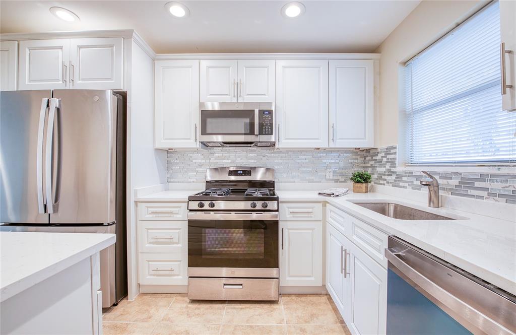 A kitchen with white cabinets, stainless steel appliances, a tiled backsplash, and light-colored countertops — 5940 30TH AVENUE S UNIT 115, GULFPORT, FL