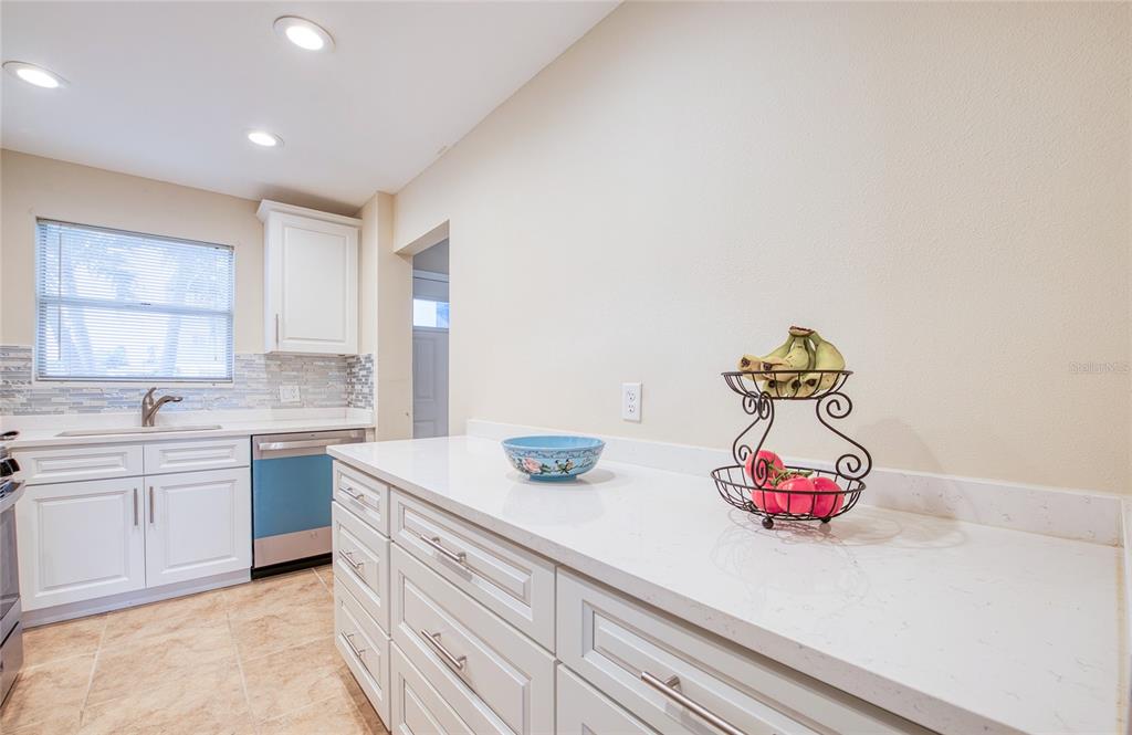 A kitchen features white cabinets, quartz countertops, a blue dishwasher, and a fruit basket — 5940 30TH AVENUE S UNIT 115, GULFPORT, FL