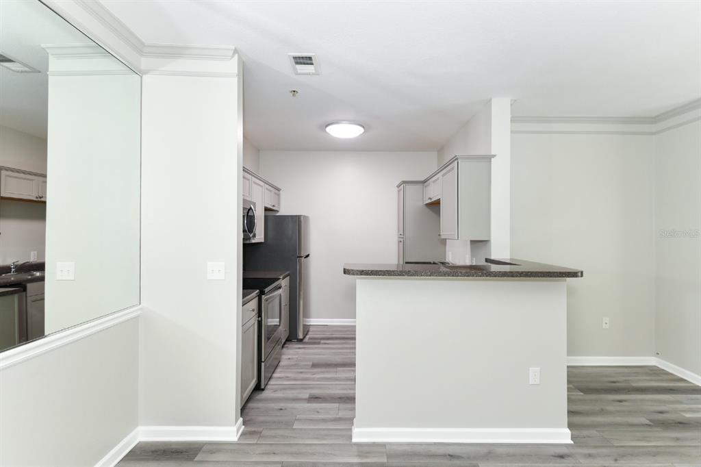 A kitchen with grey cabinets, stainless steel appliances, and a breakfast bar overlooks a room — 4802 51ST STREET W UNIT 1009, BRADENTON, FL