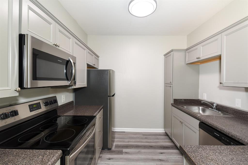 A galley kitchen features gray cabinets, dark countertops, stainless steel appliances, and wood-look flooring — 4802 51ST STREET W UNIT 1009, BRADENTON, FL