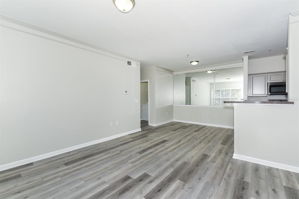 An open-concept living area features light gray walls, wood-look flooring, and a mirrored kitchen wall — 4802 51ST STREET W UNIT 1009, BRADENTON, FL