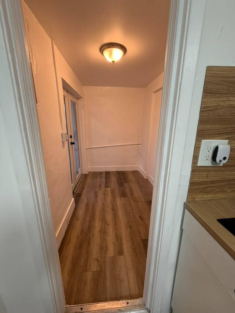 A narrow hallway with wood-look flooring leads to a glass door under a ceiling light — 2137 NW 1st Terrace, FL 33125, FL