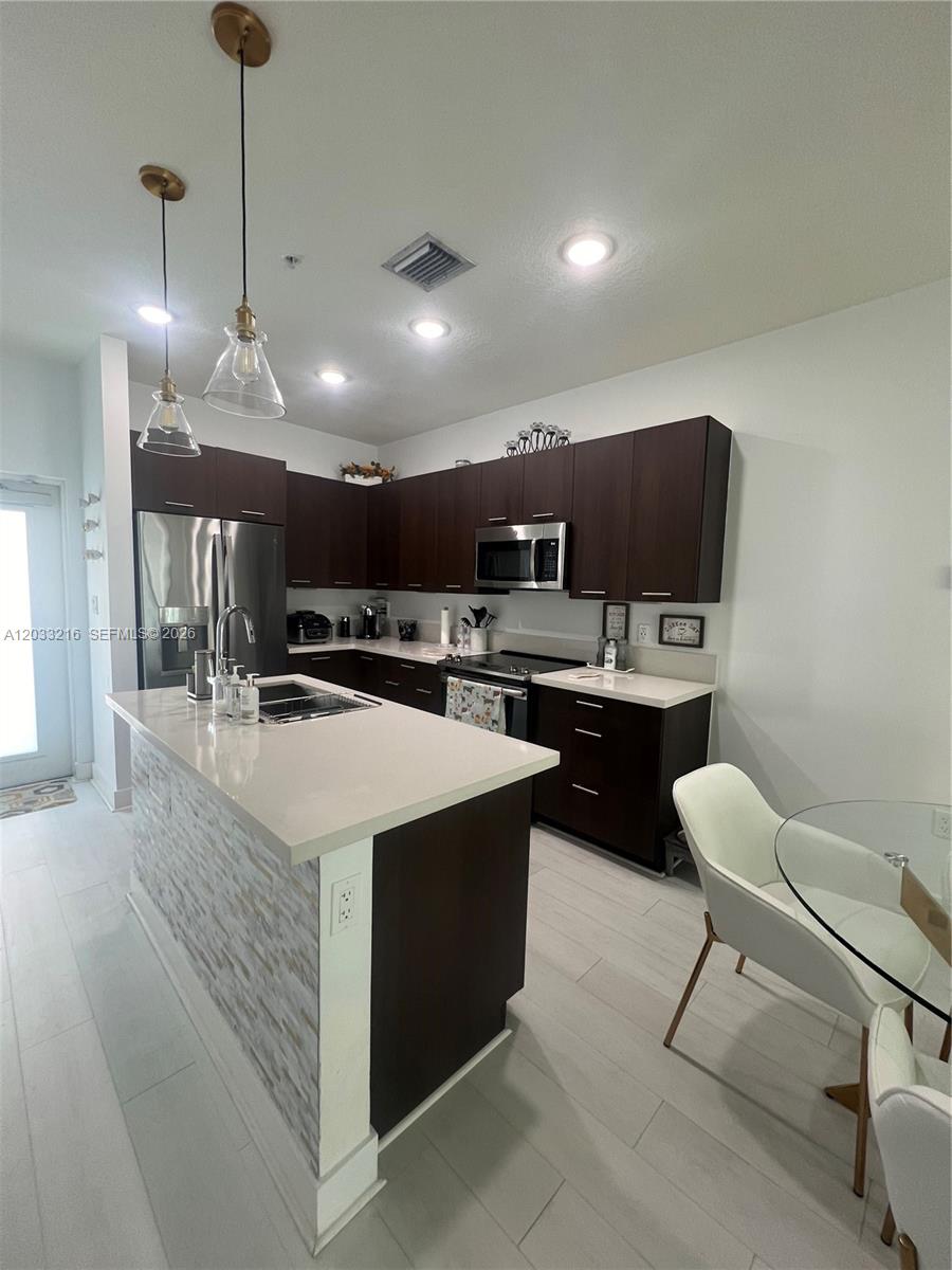 A modern kitchen features dark wood cabinets, white countertops, a central island, and stainless steel appliances — 4670 NW 84th Ave # 32, Doral FL 33166, DORAL, FL