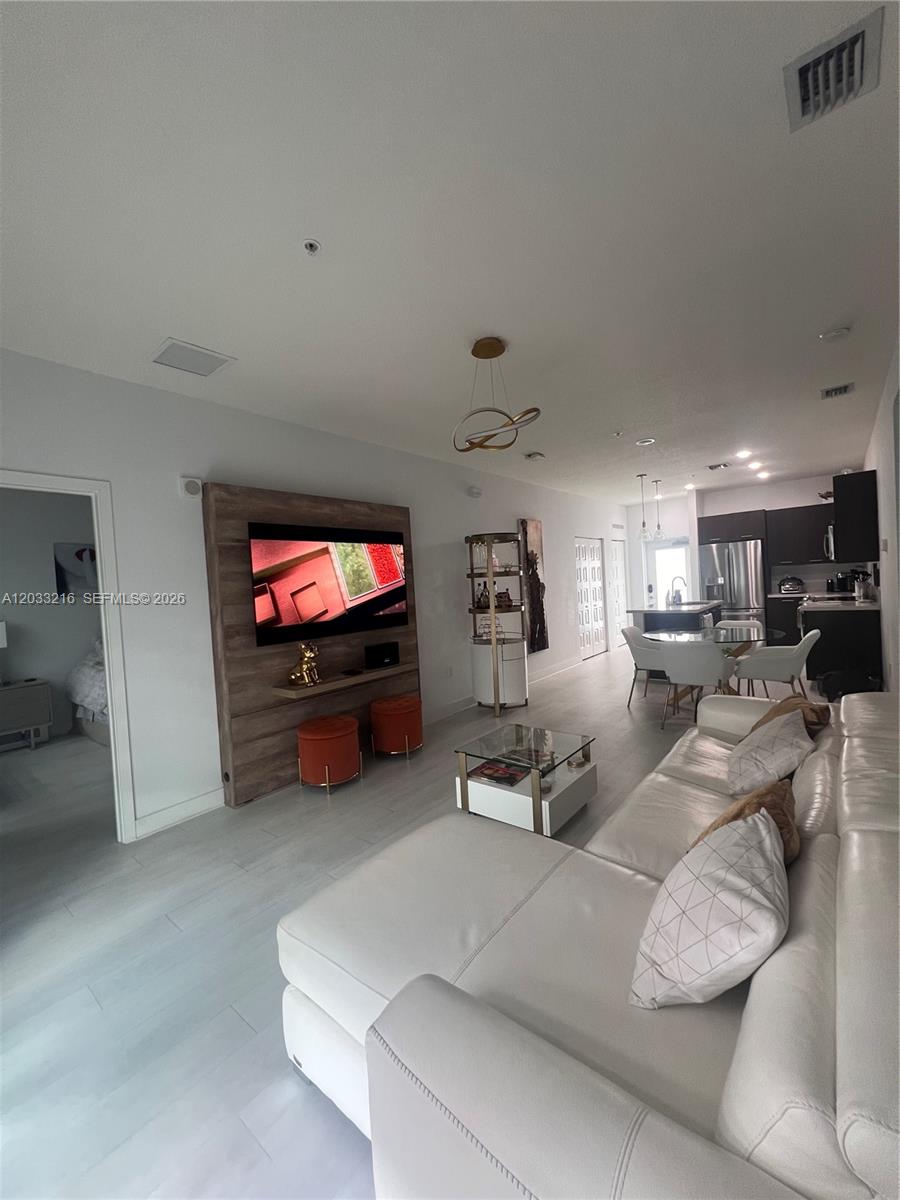 A modern living room features a white sectional sofa, wood-paneled media wall, and open kitchen — 4670 NW 84th Ave # 32, Doral FL 33166, DORAL, FL