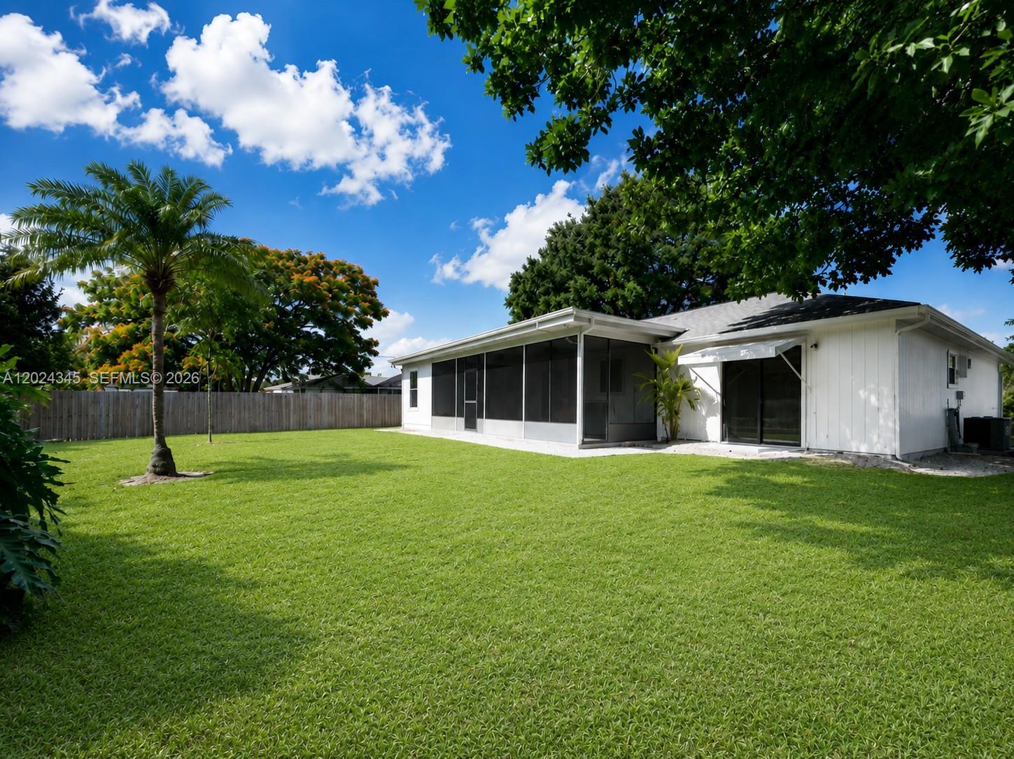 A backyard features a green lawn, a palm tree, and a house with a screened porch — 112 SE Vin Rose Cir, Palm Bay FL 32909, PALM BAY, FL