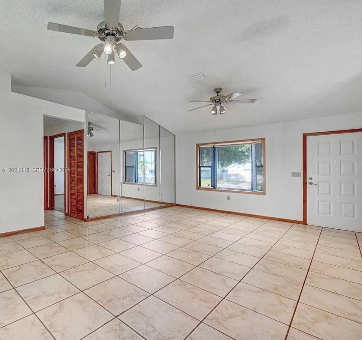 An empty room features tiled floors, two ceiling fans, a mirrored wall, and a door — 112 SE Vin Rose Cir, Palm Bay FL 32909, PALM BAY, FL